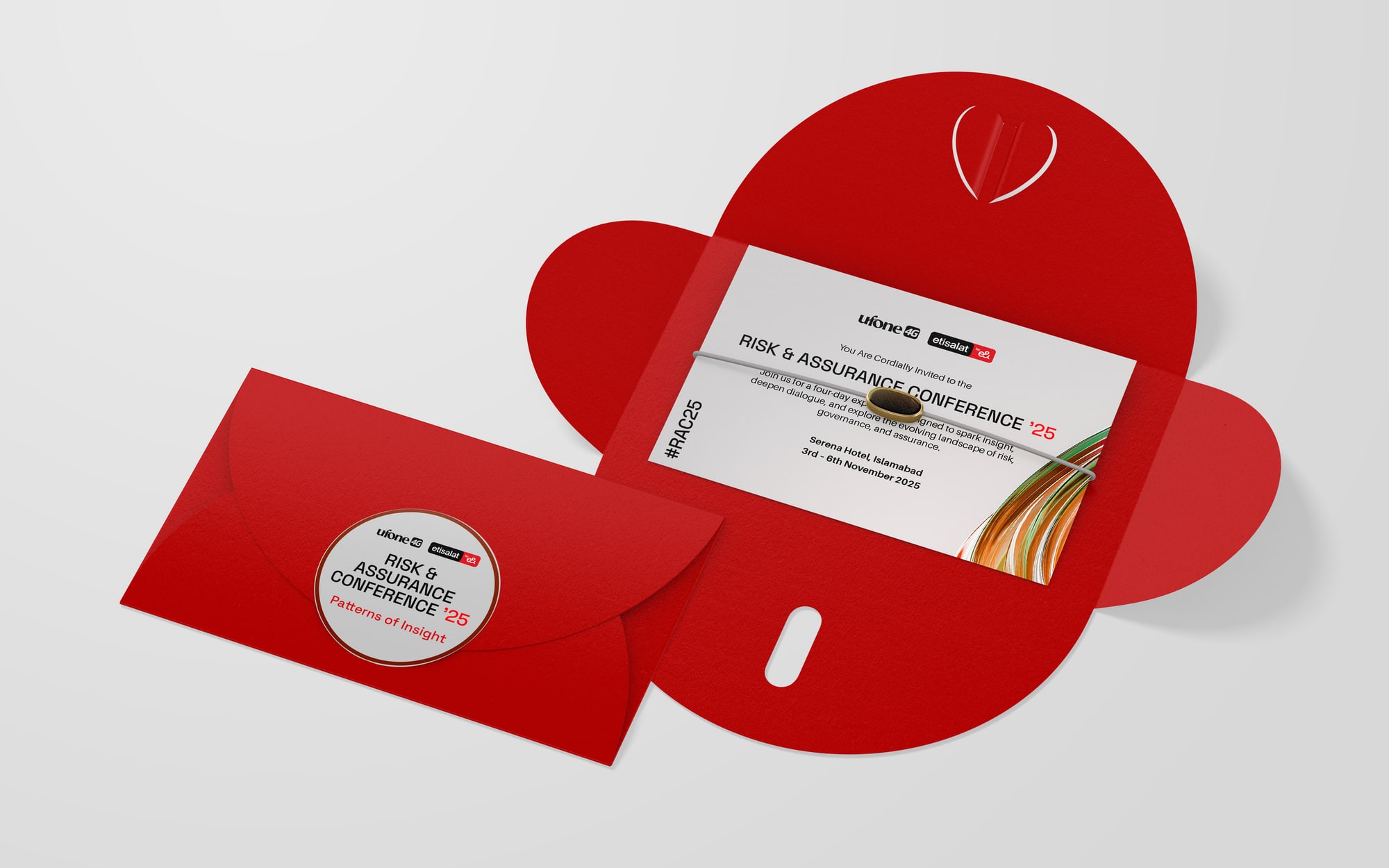 A red die-cut invitation envelope lying open with a white card inside carrying the title and the ribbon, a second envelope sealed with a round sticker
