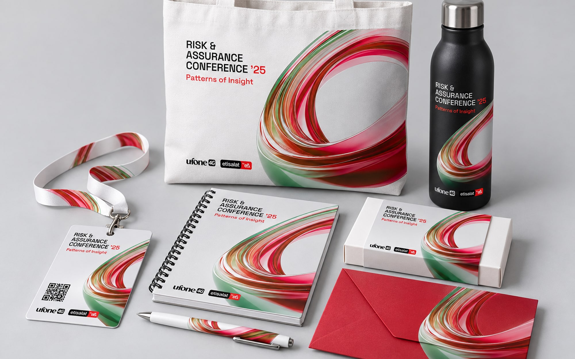 The delegate kit laid out: a white tote, a lanyard and name badge, a notepad, a pen, a black bottle, a box of chocolates and a red envelope, all carrying the ribbon