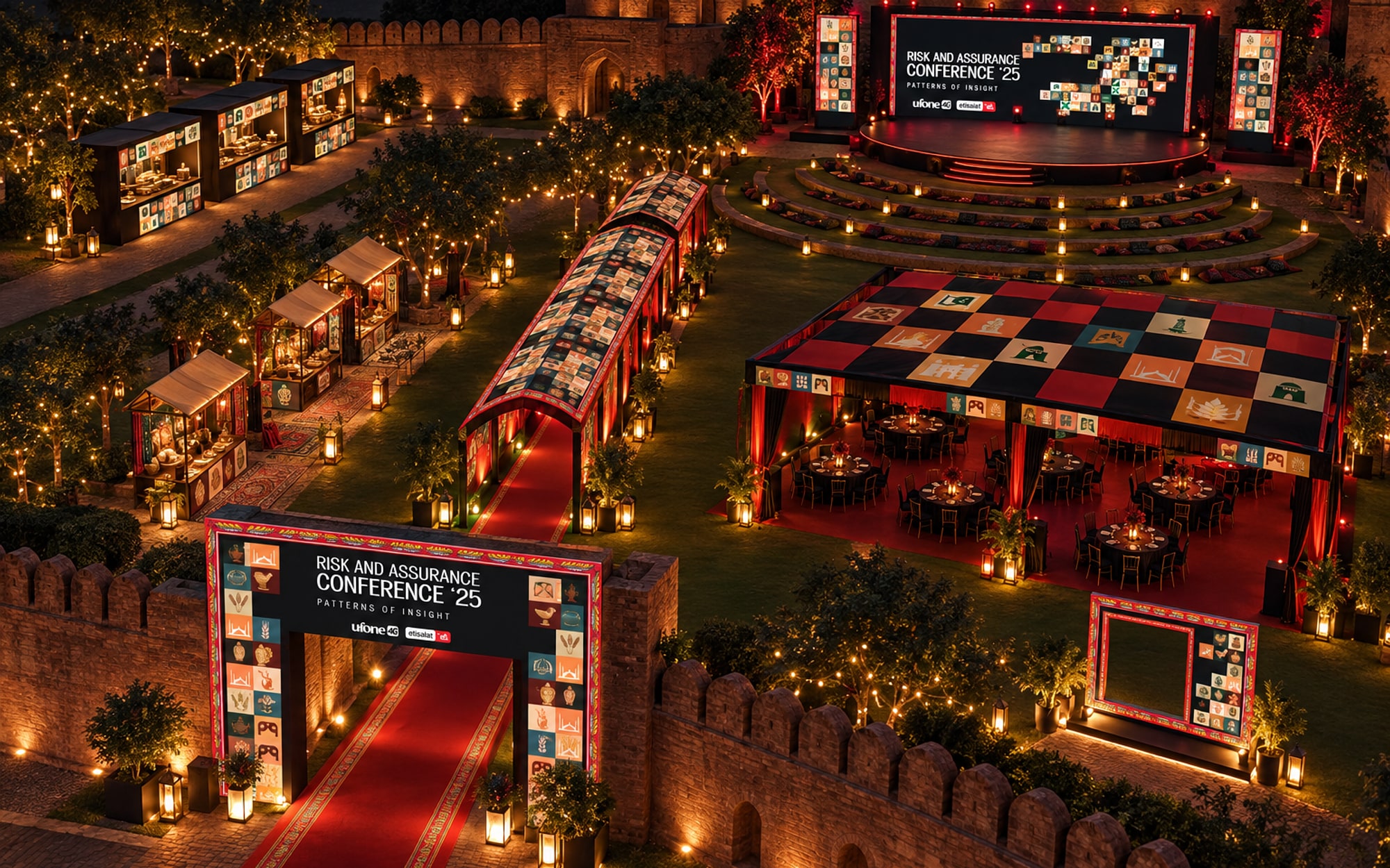 An aerial view of the fort grounds at night: the gate and red carpet, the stage and its terraces, the dining canopy, the stalls and the bazaar lane