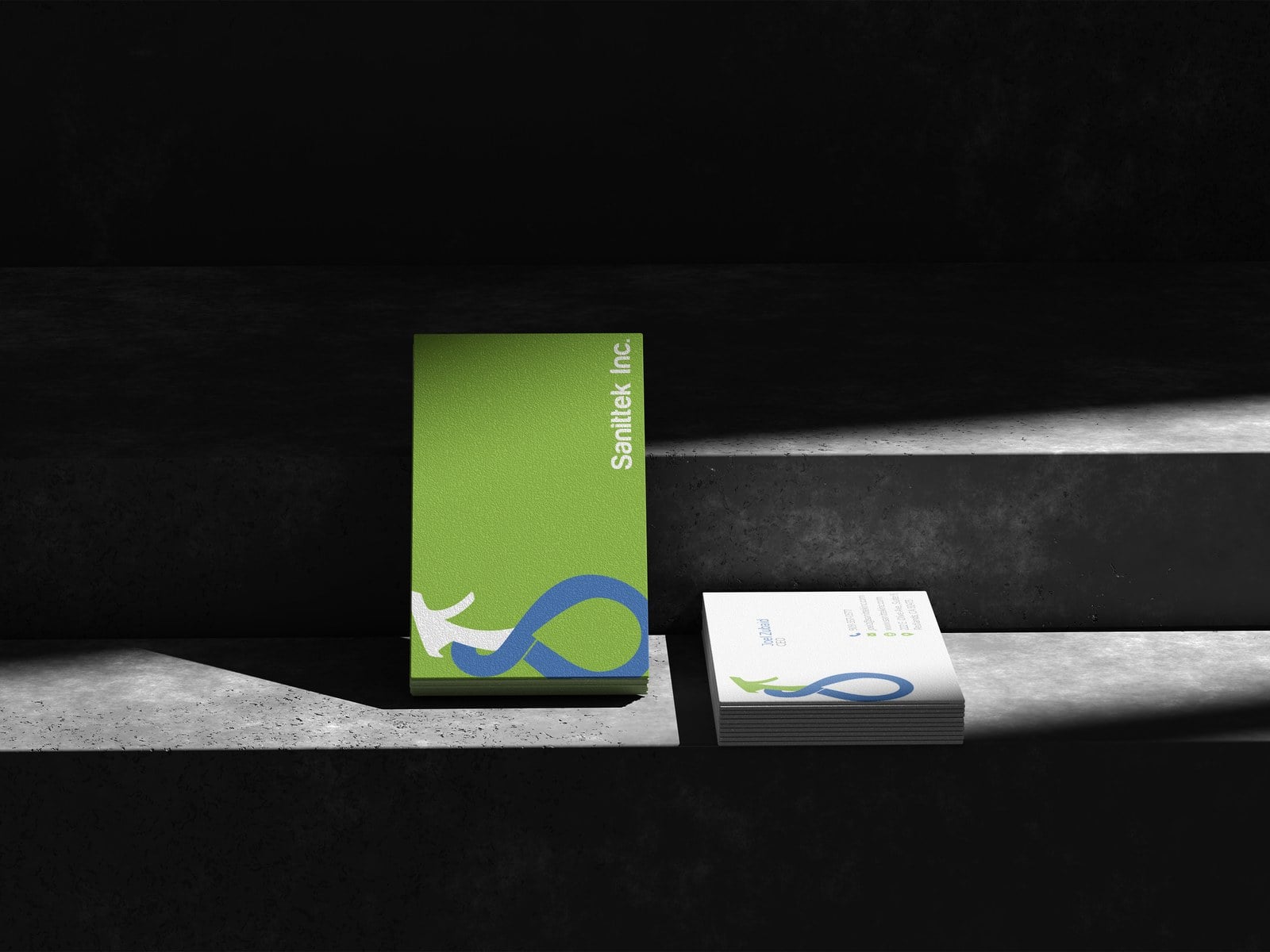 Sanittek business cards, green and white, standing on a concrete ledge in hard directional light.